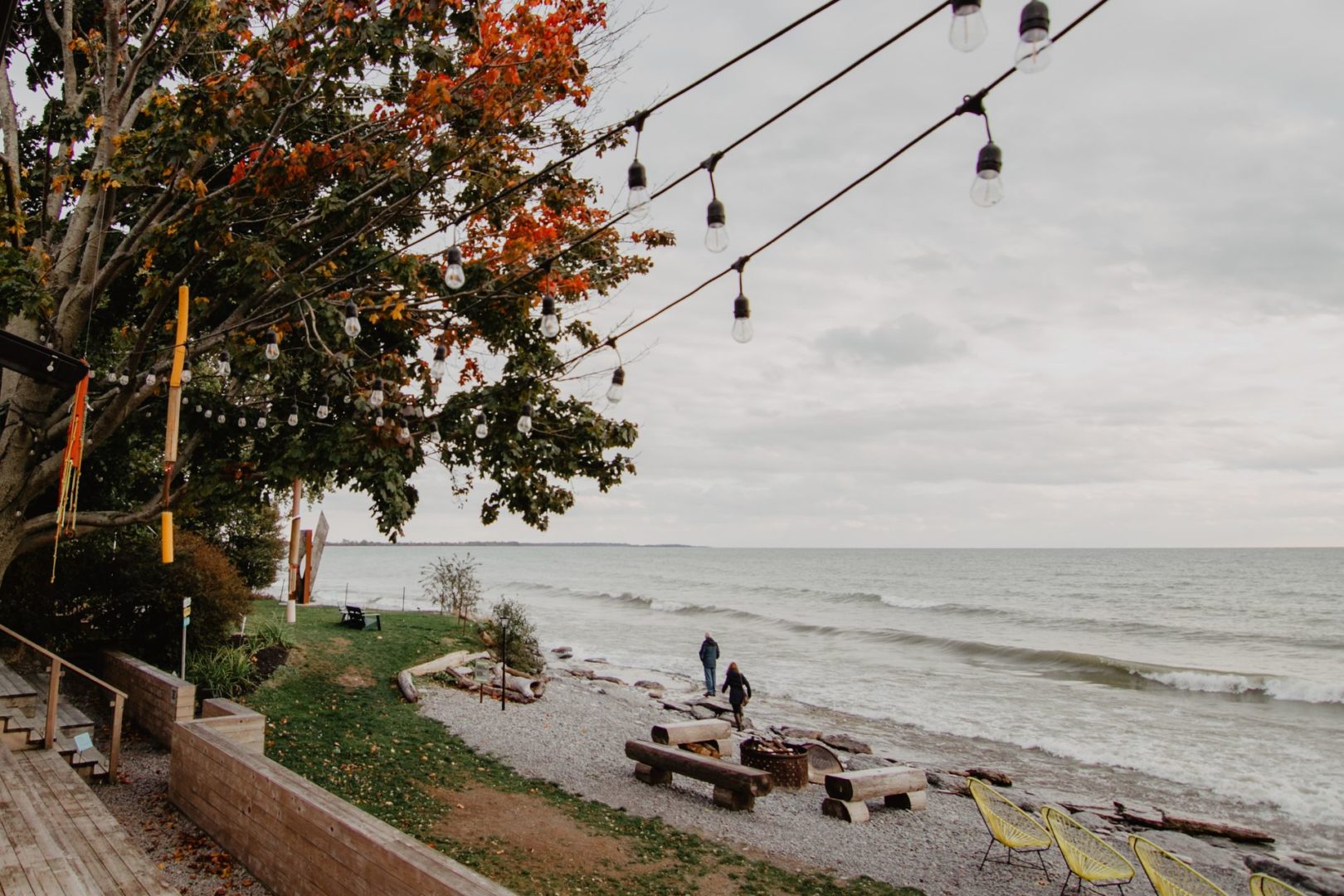 Two people on a small beach, with string lights hanging on a tree above.
