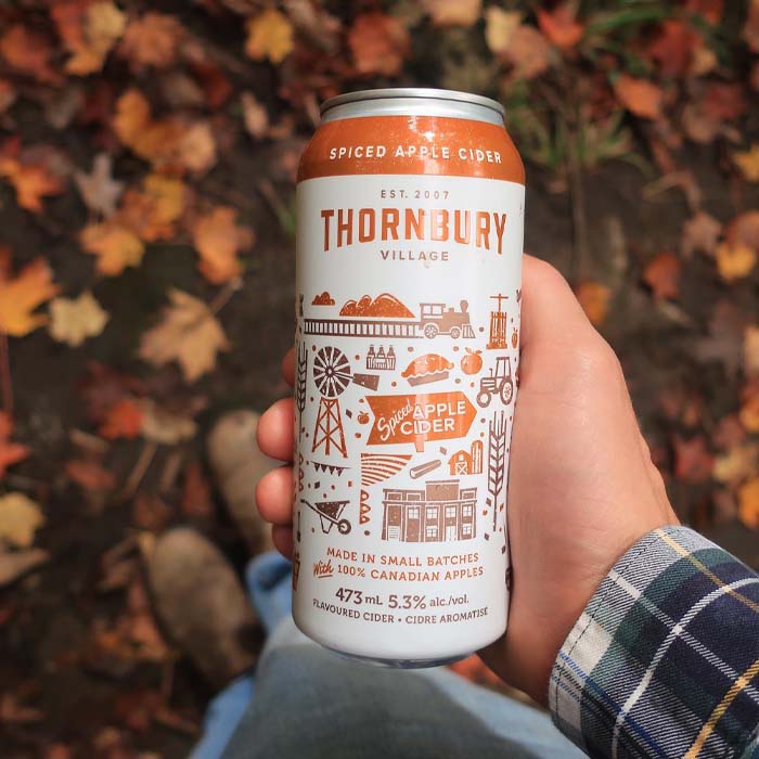 Thornbury Spiced Apple Cider can in hand in front of fall leaves