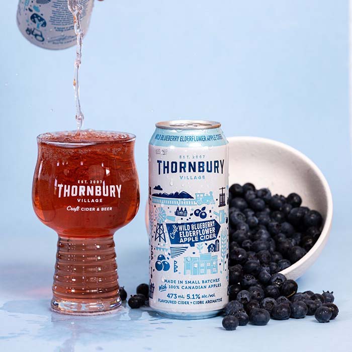 Thornbury wild blueberry and elderflower apple cider being poured into a glass surrounded by blueberries
