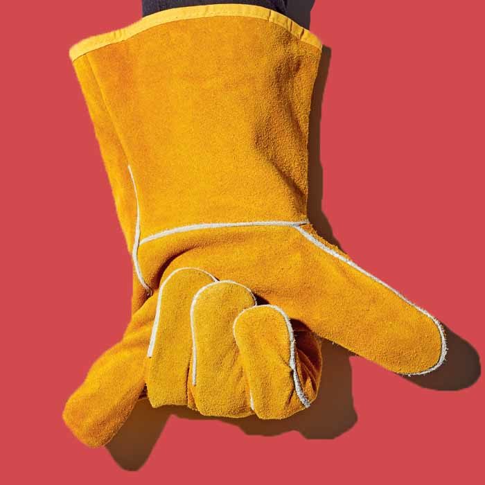 A hand wearing a yellow Mastercraft leather welding glove against a red background.