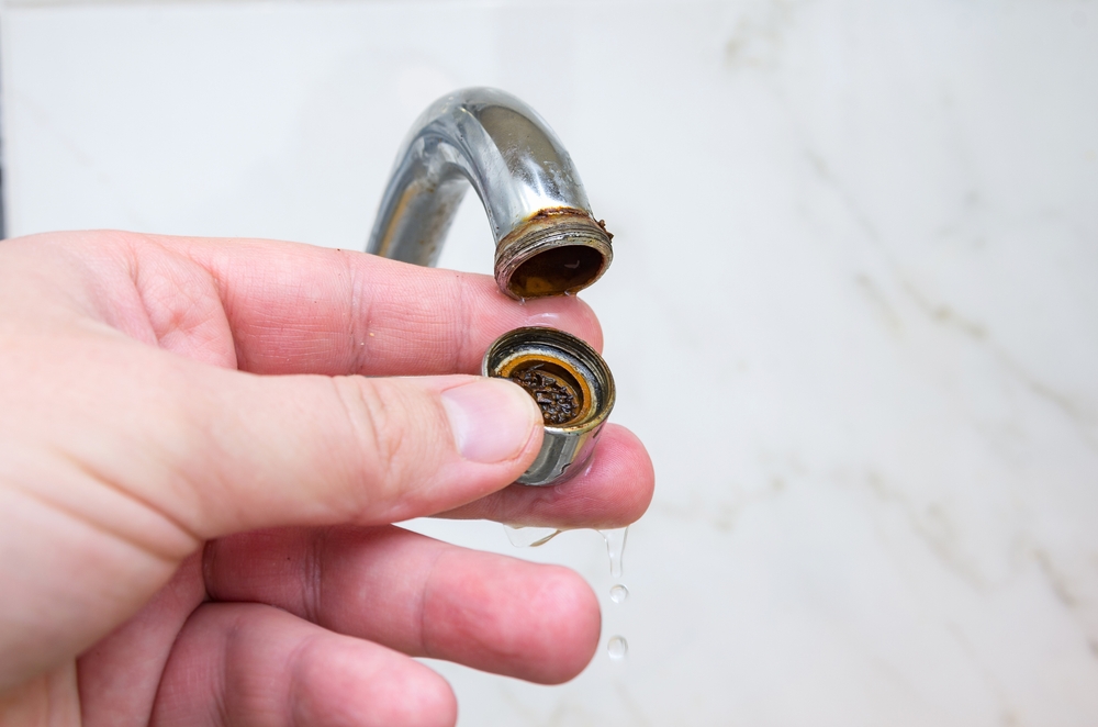 A hand removing a clogged aerator from a kitchen faucet