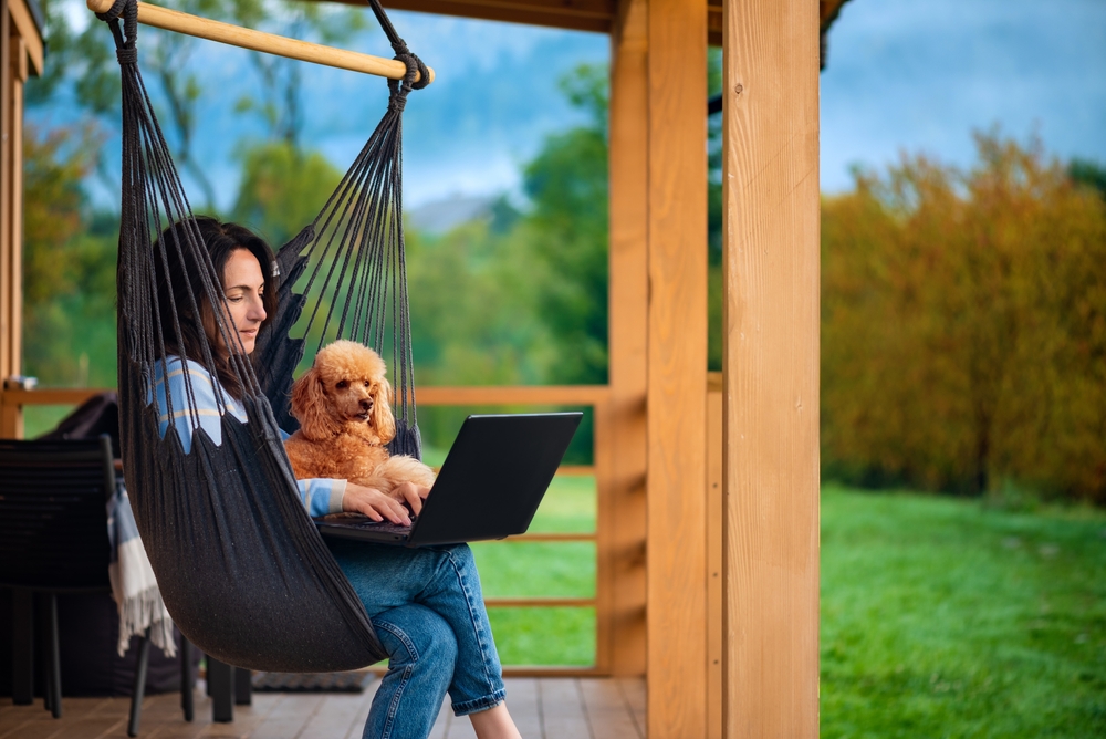 A woman on her deck working on a laptop, next to her dog.