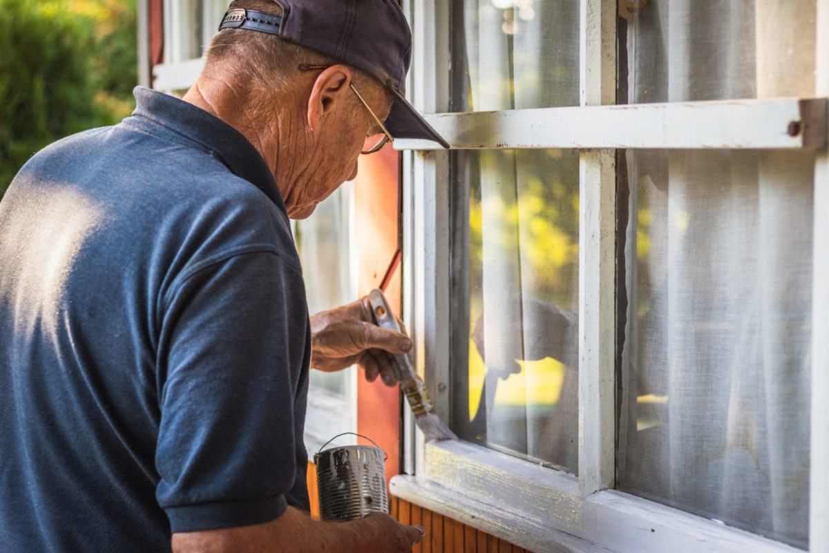 Man repairing window frame on a maturing cottage.
