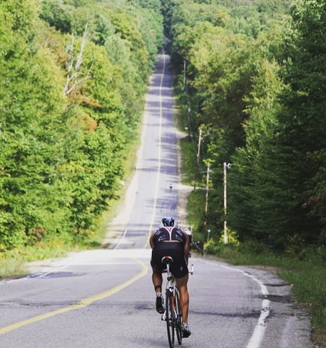 A biker on a road surrounded by woods in Muskoka