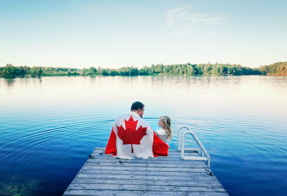A father and daughter sitting on the dock, wrapped in a Canadian flag