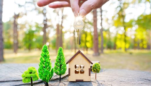 A hand dangling a key over a miniature cabin