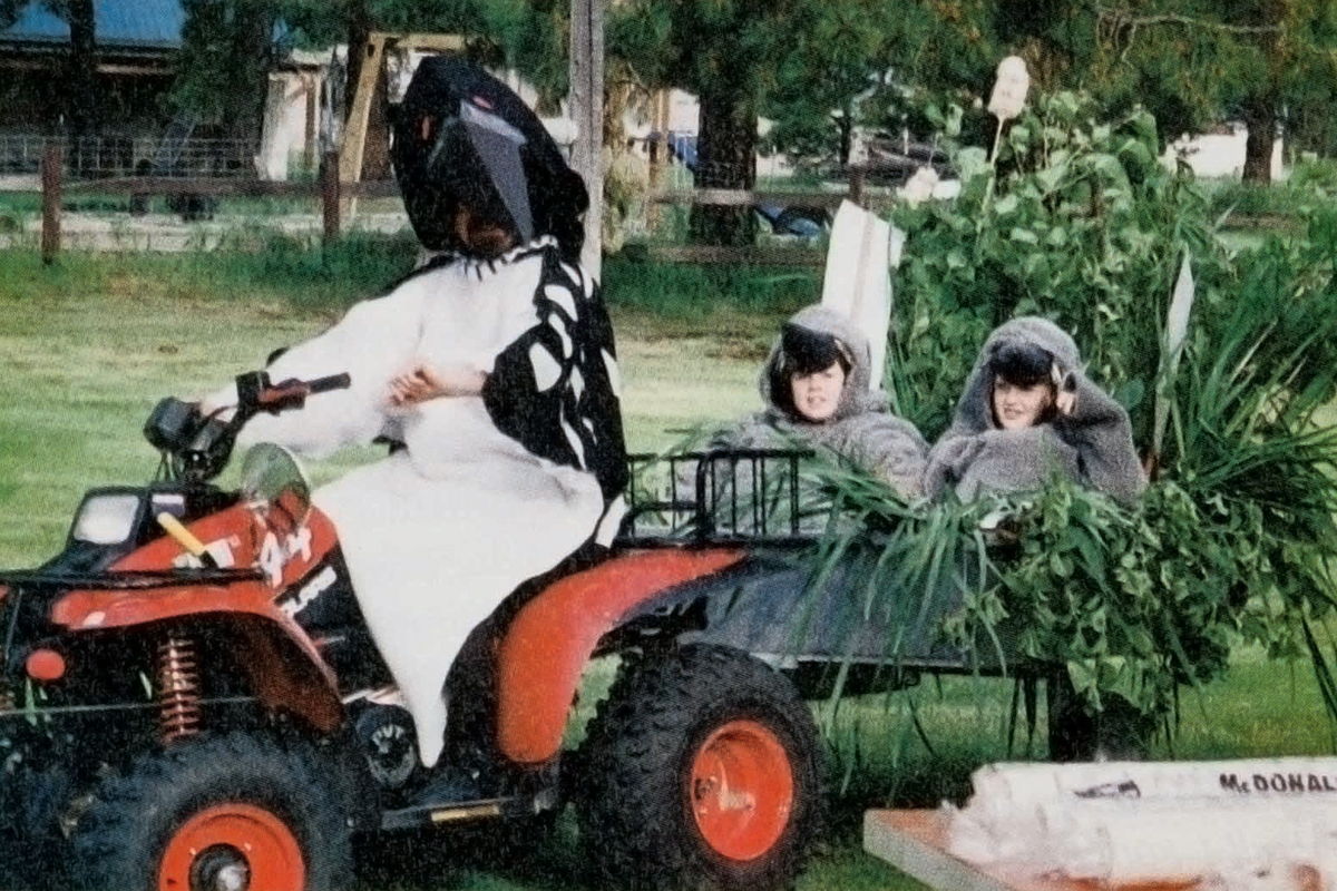 a person dressed in a loon costume riding an ATV while towing two kids also dressed as loons
