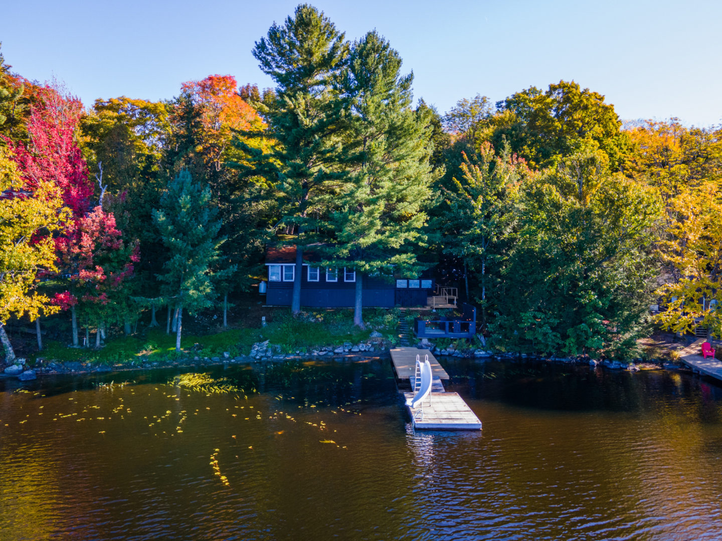 A small cottage set back from the shoreline of a lake, with a long narrow dock out front.