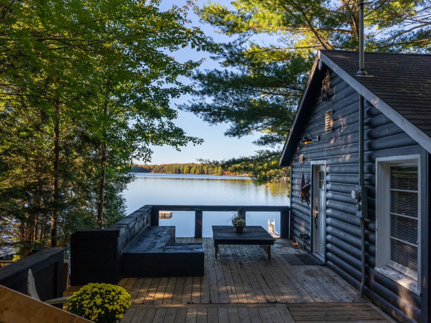 A large deck that branches off of a cottage, with a lake in the background.