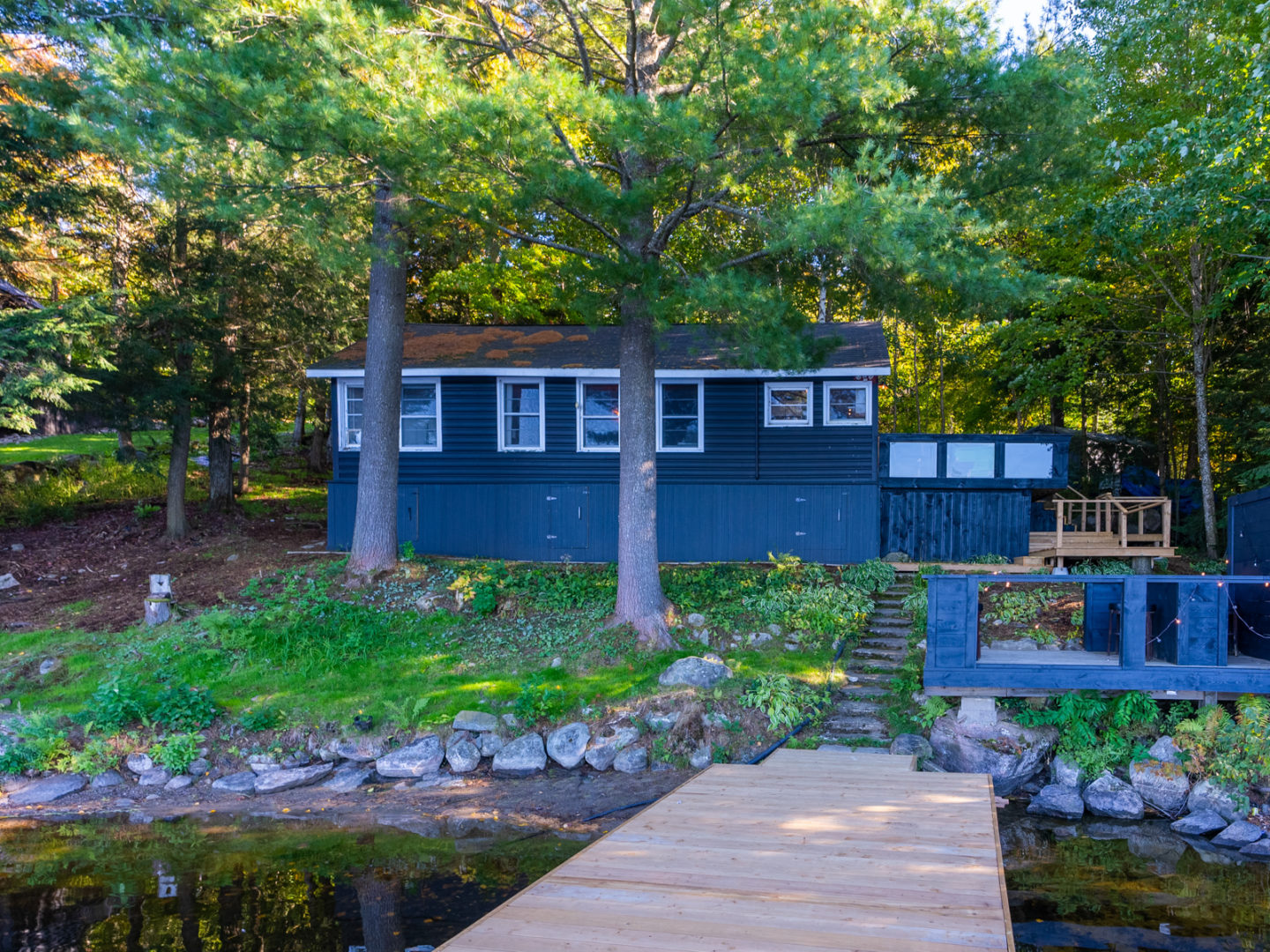 A cottage set back from the water, with a dock extending into a lake.