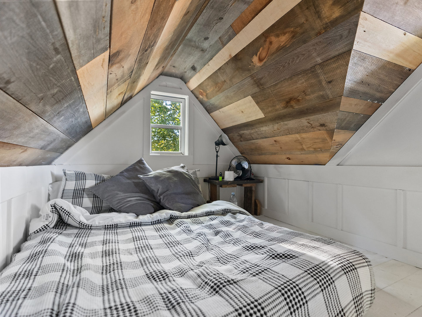 A bed in a narrow loft space with flannel sheets.