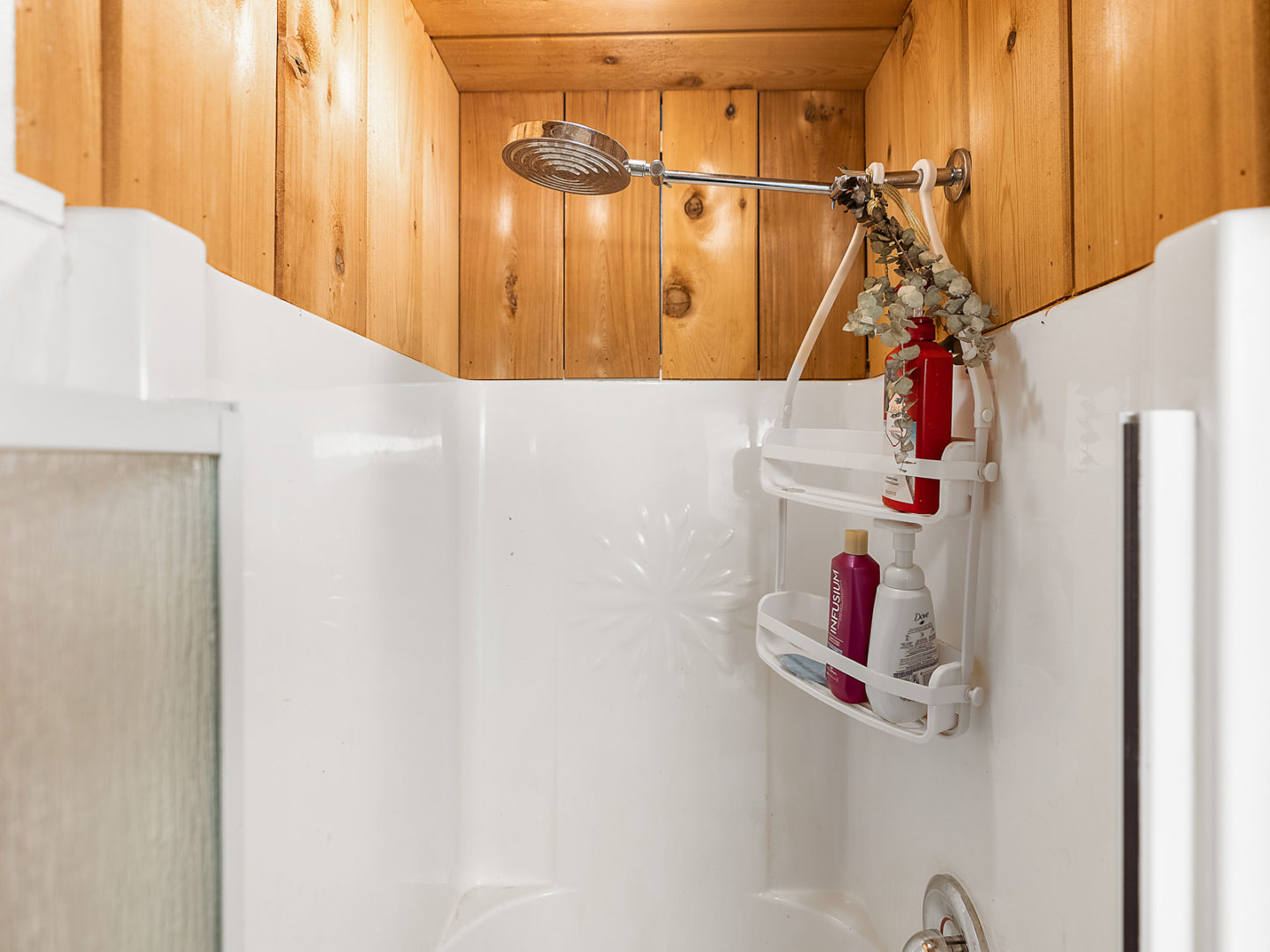 A small shower with a wood panelled ceiling.