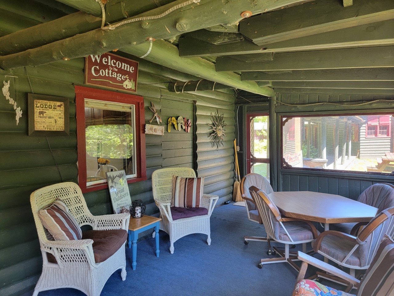 A bright screened-in porch with wicker chairs and a sign that says "Welcome to the Cottage."