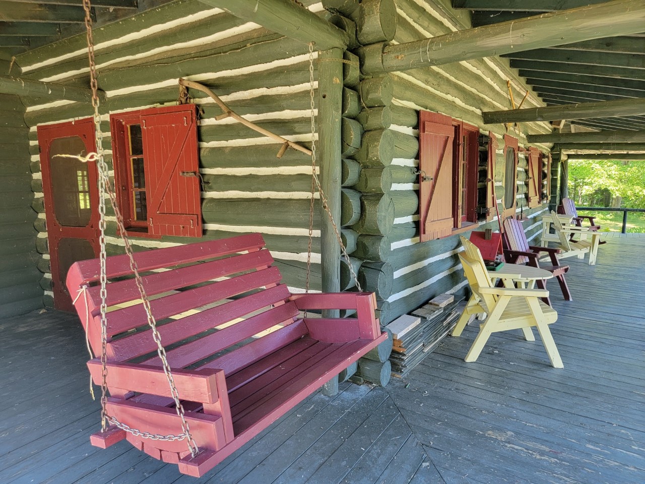 The corner of a covered wrap-around porch, with a rustic wooden porch swing.