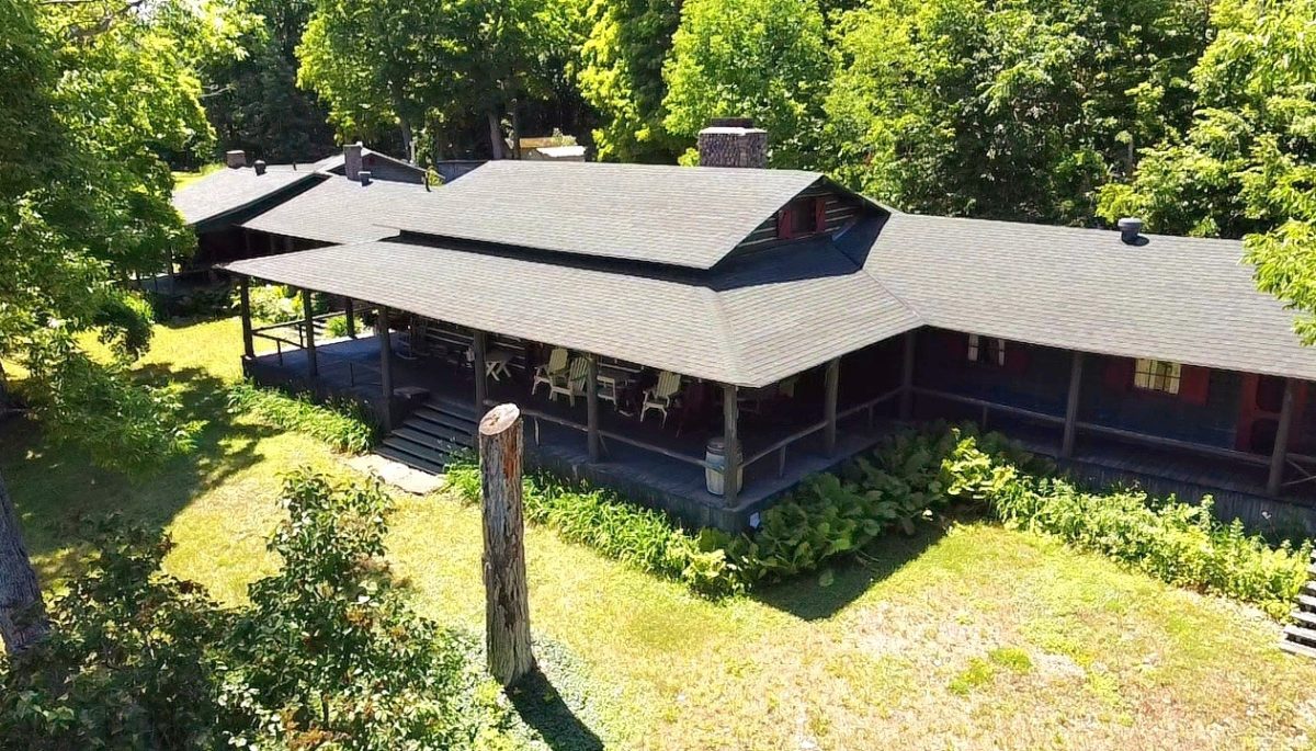 Overhead shot of a large single-story cottage, which has a large covered front porch and an expansive lawn.