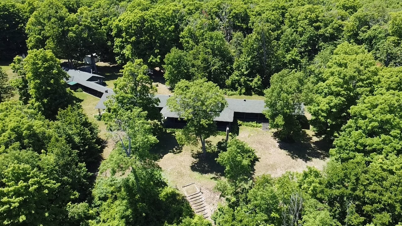 Overhead shot of a large one-story cottage surrounded by trees.