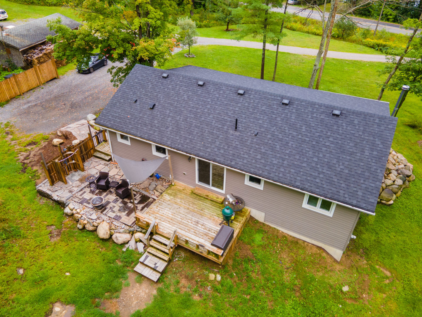The back of a one-story cottage with a back deck, a small patio with chairs, and an outdoor shower.