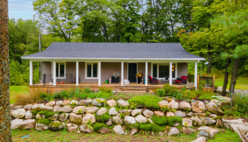 Exterior view of a one-story cottage with large front windows and a front deck spanning the house.
