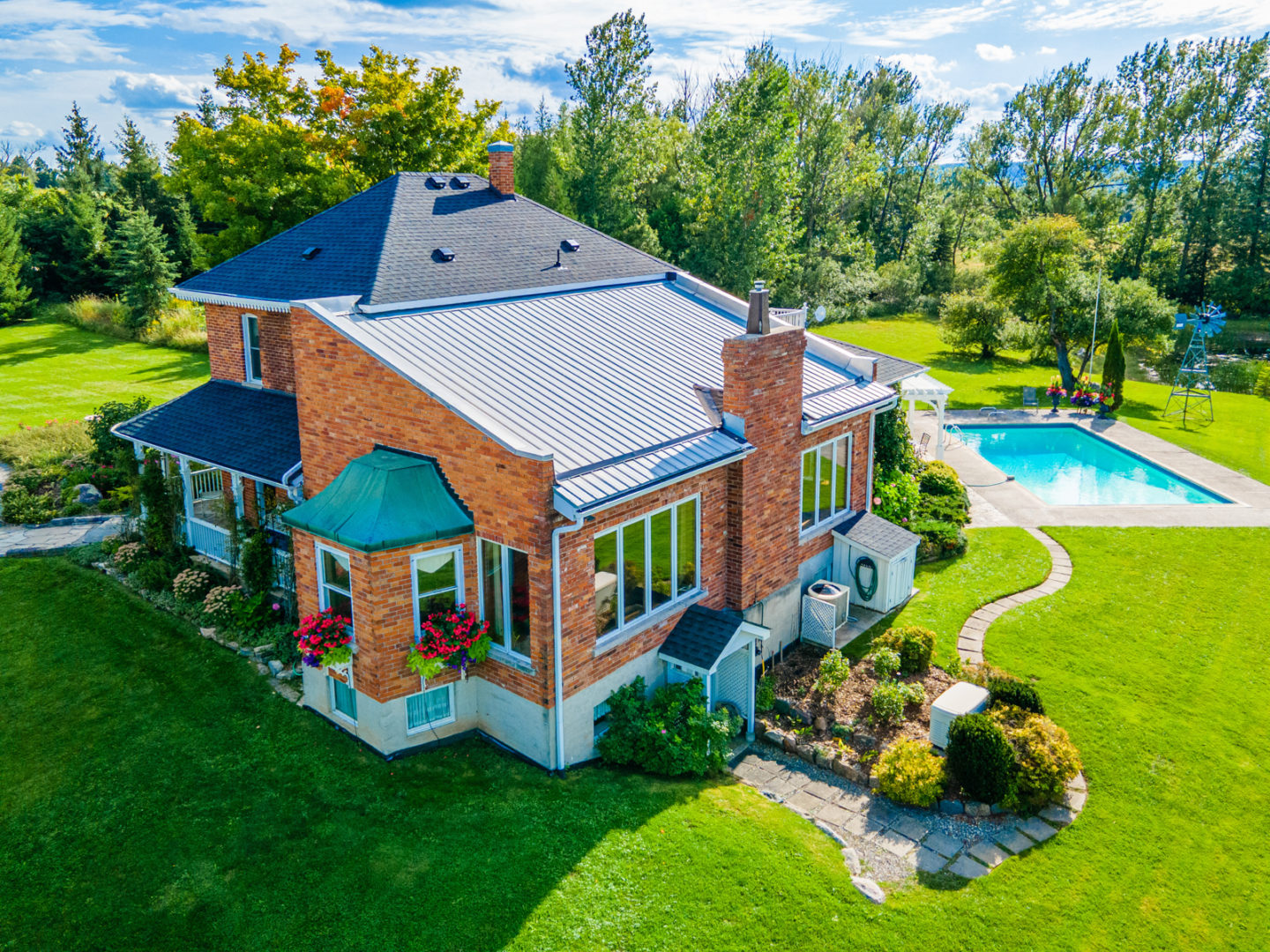 A large, red-bricked country home with a large yard and part of a pool visible in the backyard.