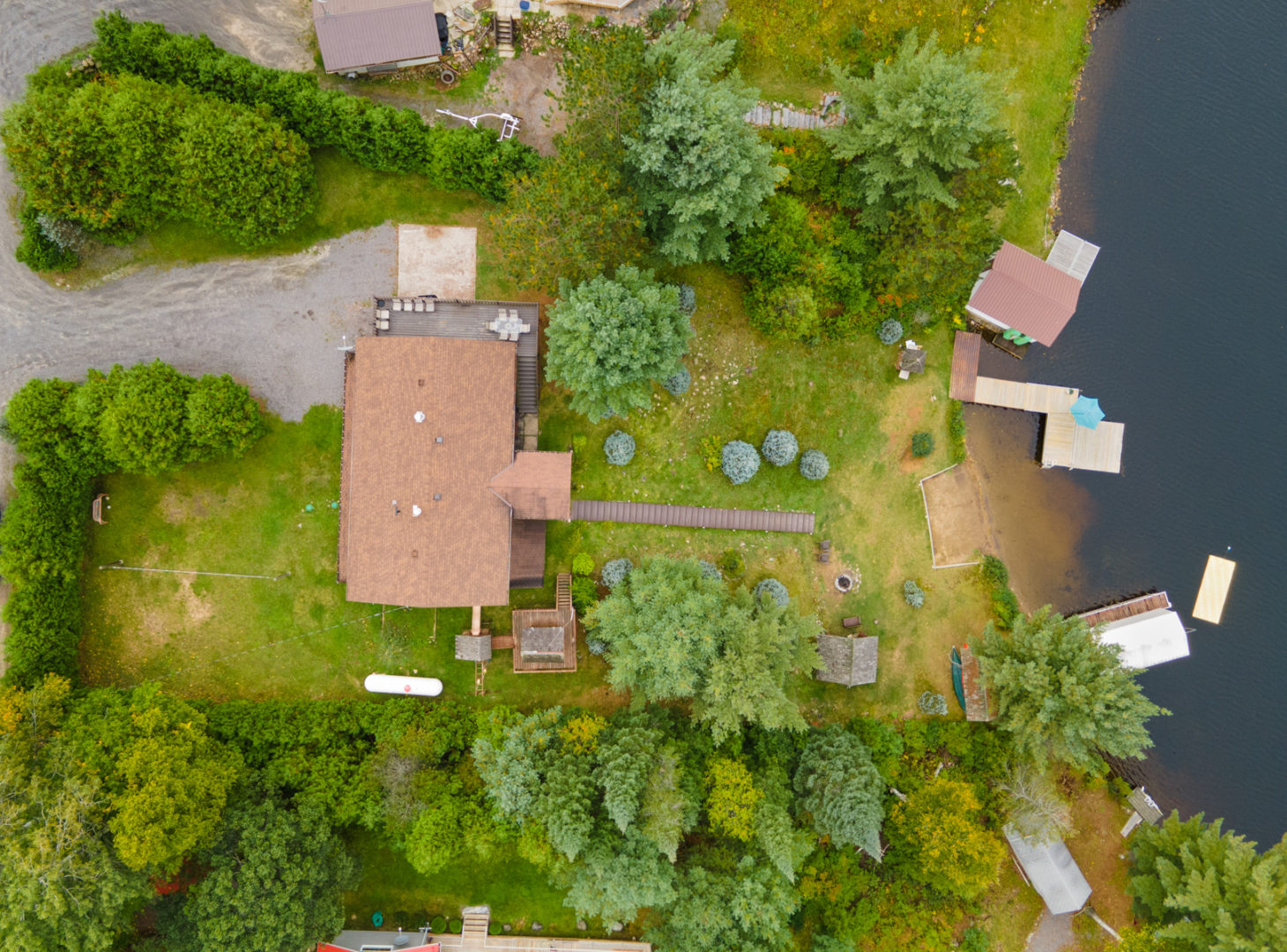Aerial view of a lakefront home, surrounded by trees on top of a hill, with a small sandy beach and a long dock down by the water.