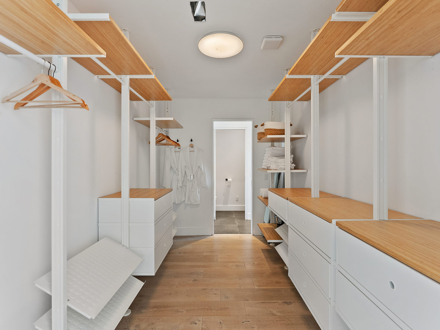 A large walk-in closet area with drawers, hanging racks, and shelving on either side.