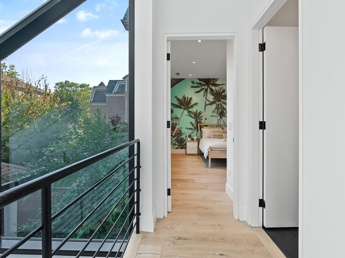 A staircase landing with a black metal railing. The entrance to a bright bedroom is straight ahead.