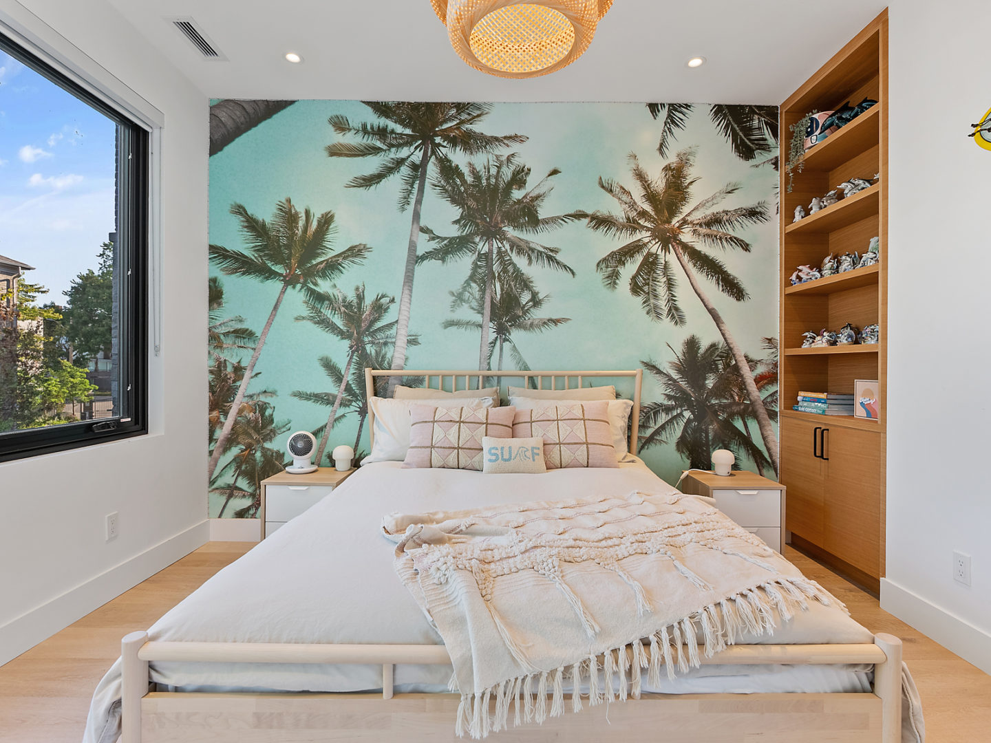 A bedroom with a large white bed and a mural of palm trees on the wall behind the bed.