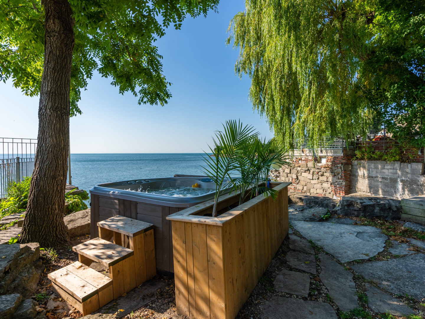 A big hot tub on a patio area in front of a lake.