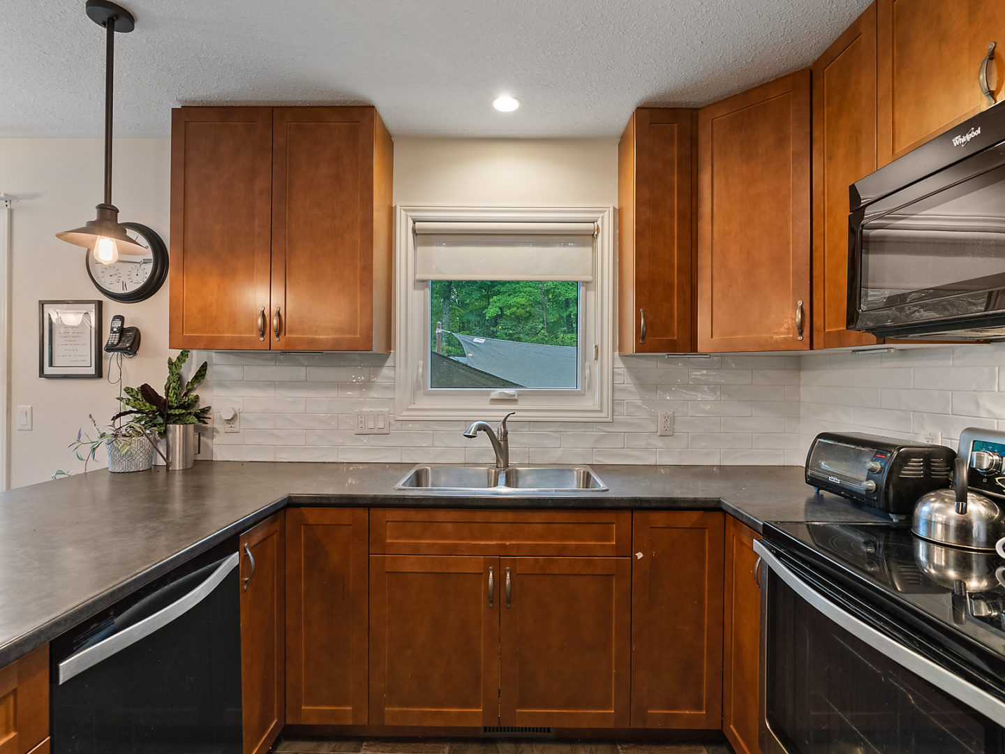 A small but updated kitchen area with warm brown cabinets, an oven, a dishwasher, and a window over a sink.