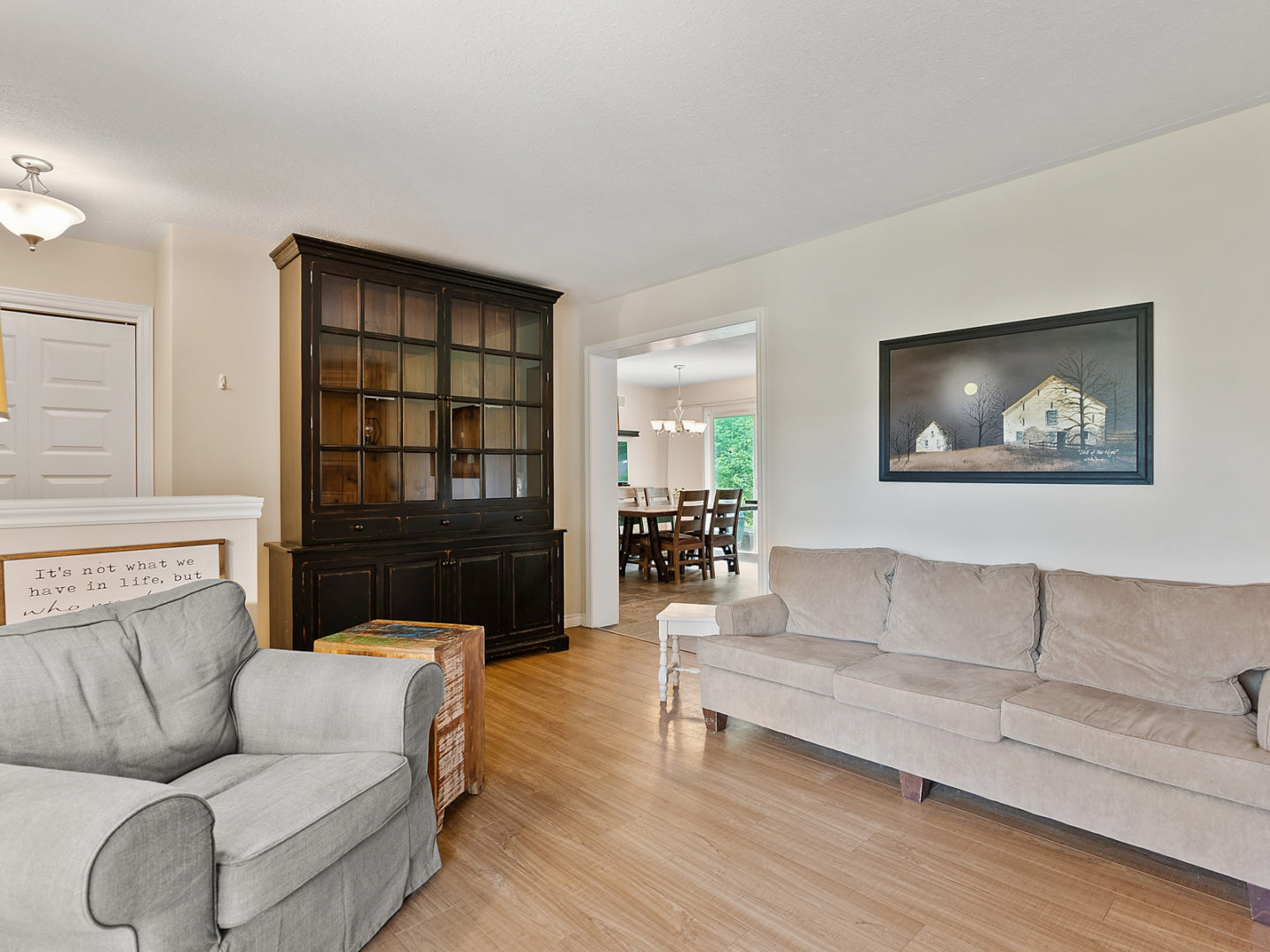 A spacious living area with hardwood floors, a couch and a chair, with a doorway leading into a dining room.
