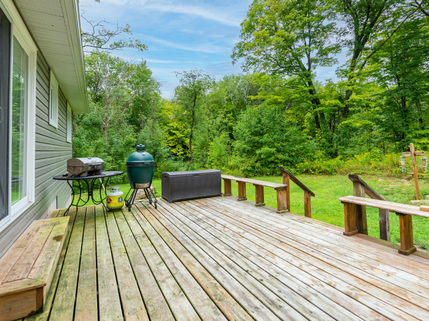 A large deck off the back of a house, with a barbecue at the end.