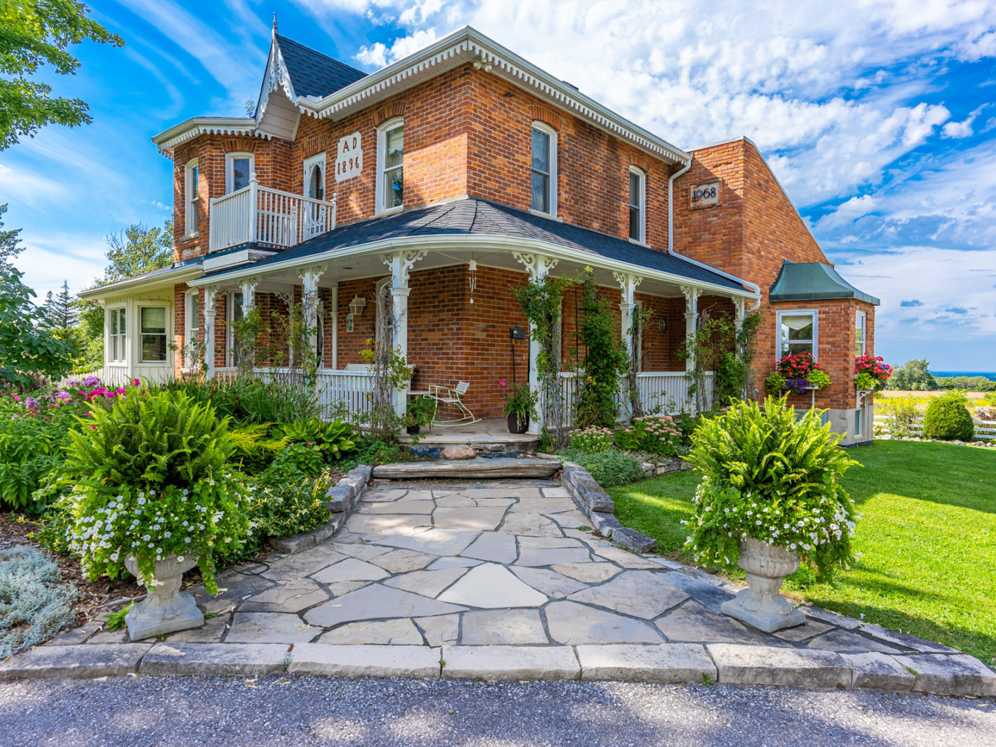 Exterior corner view of a large country estate, showing a long porch wrapping around both sides of the house.