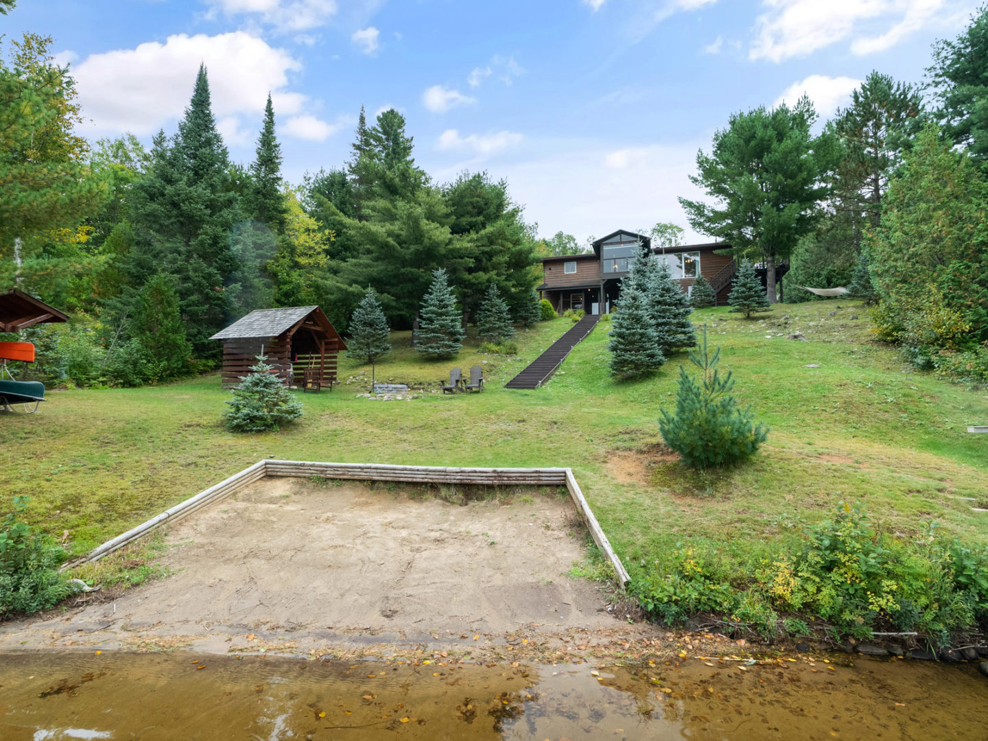 A small sandy beach on a lake, with a large home in the background at the top of a hill.
