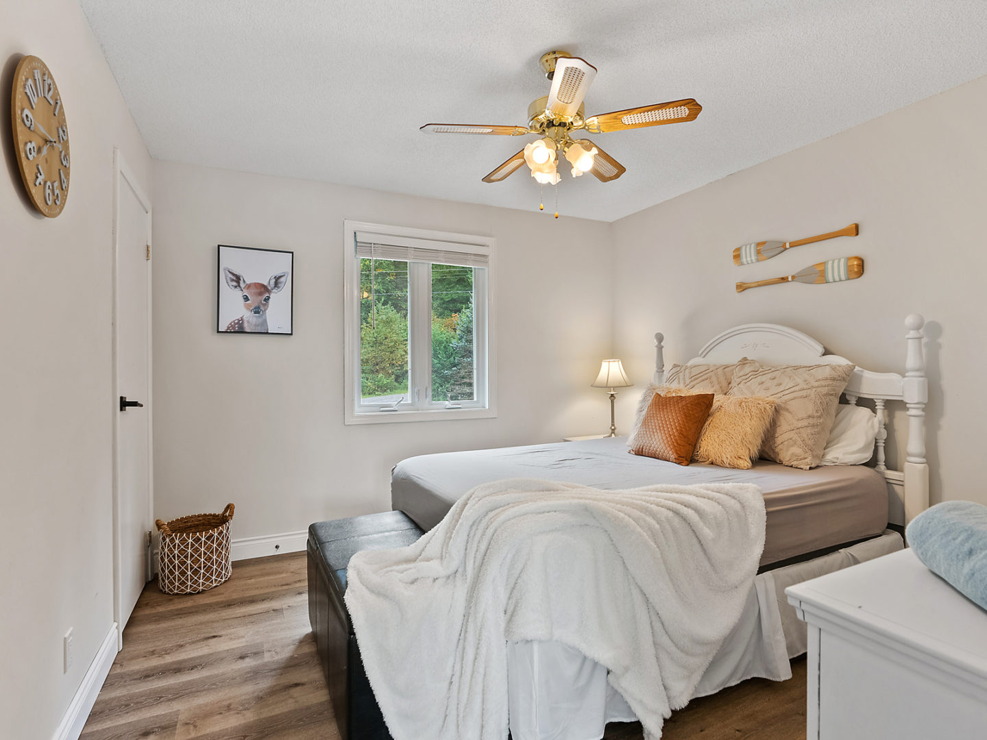 A bedroom with a large bed, wood floors and decorative canoe paddles on the wall above the bed.