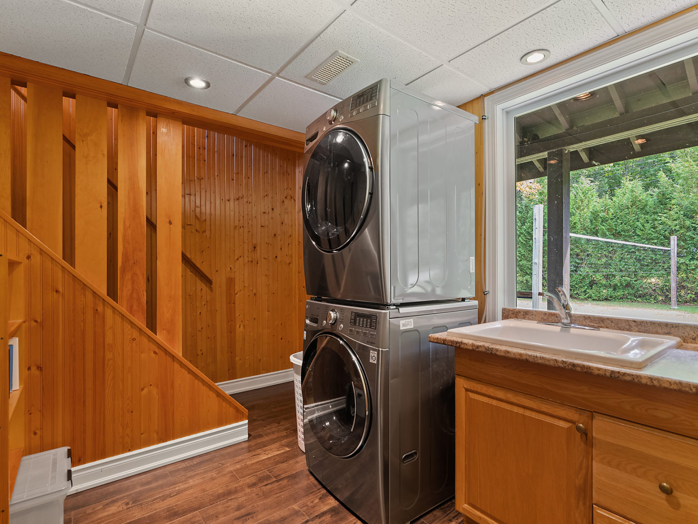 A ground-floor area with a stacked washing machine and dryer in front of a staircase leading up.