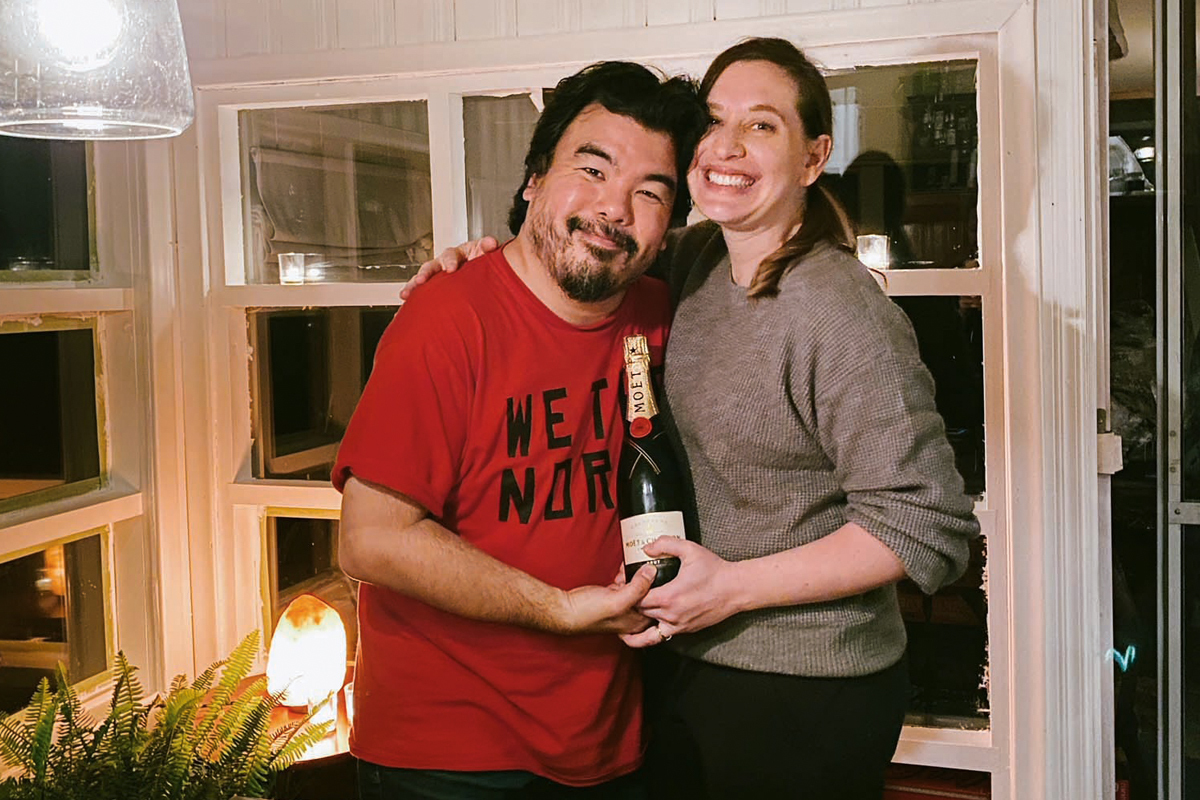 couple Jen Pogue and Warren Sonoda stand together in the sunroom at the their cottage