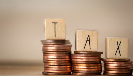 The word TAX spelled out in wooden cubes, stacked on coins