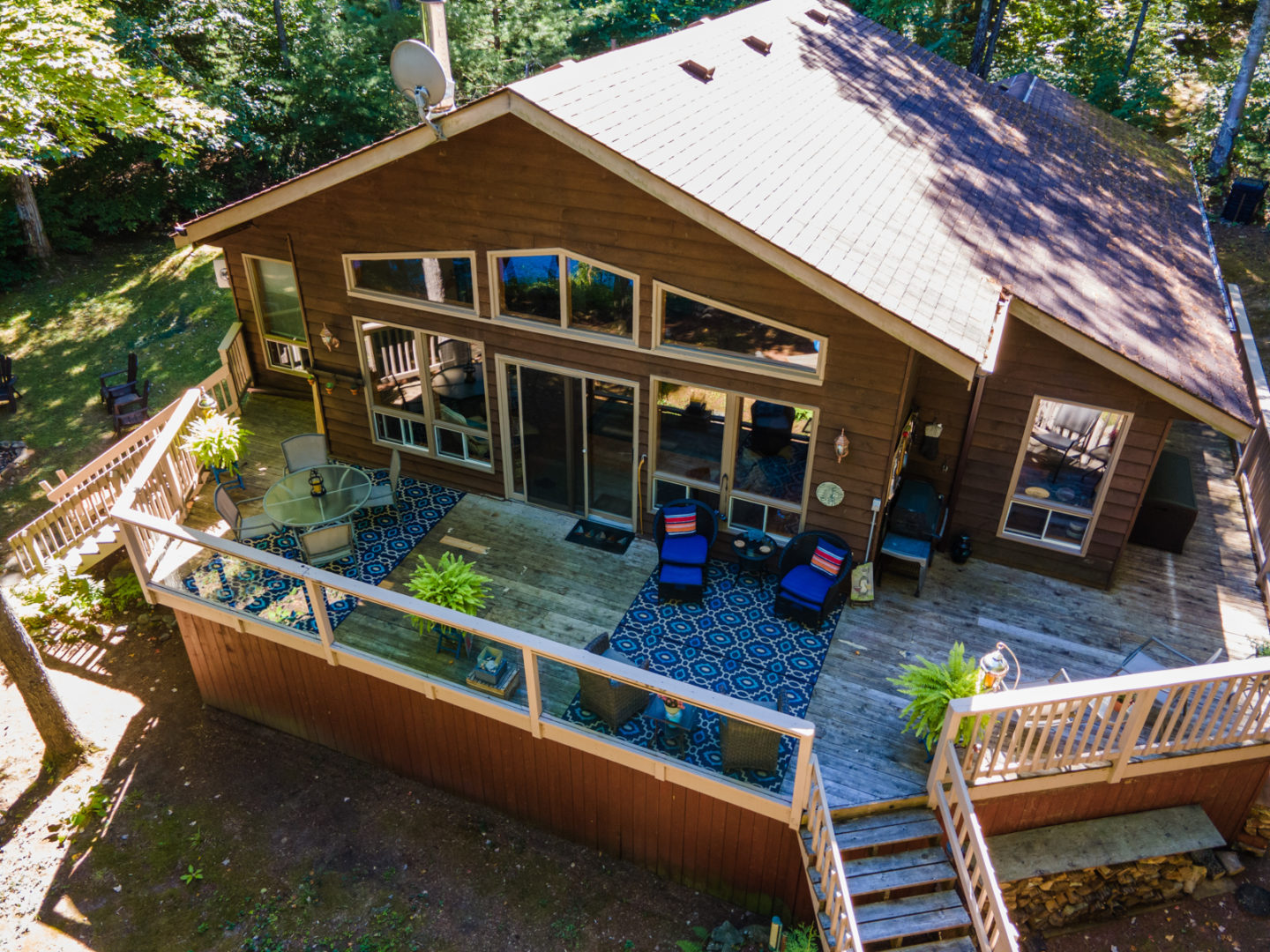 Overhead view of a large deck branching off a cottage with floor-to-ceiling windows.