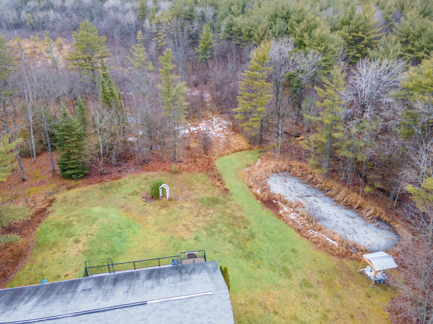 The backyard of a rural home with a large grassy space, lots of trees, and a private pond.