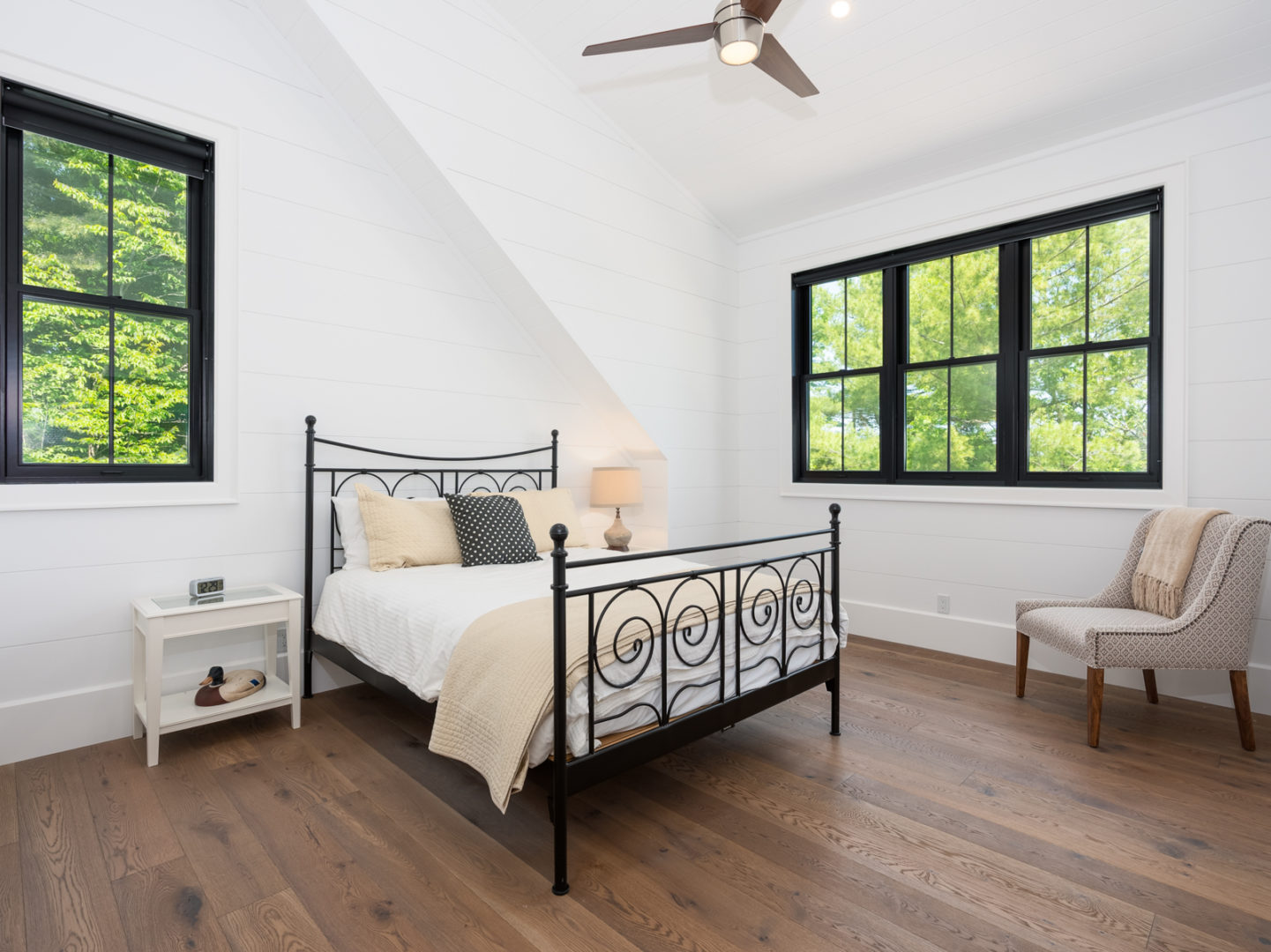 A bedroom with dark wooden floors, a large window, and white walls.