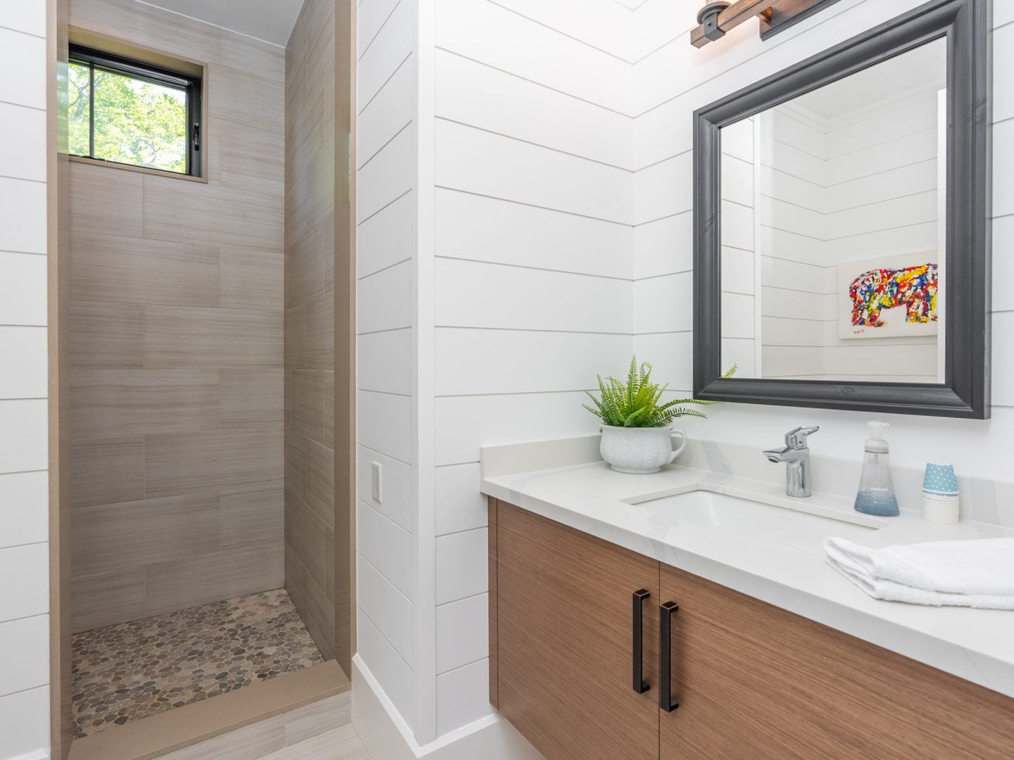 A modern bathroom with a small mirror above a sink and a shower.