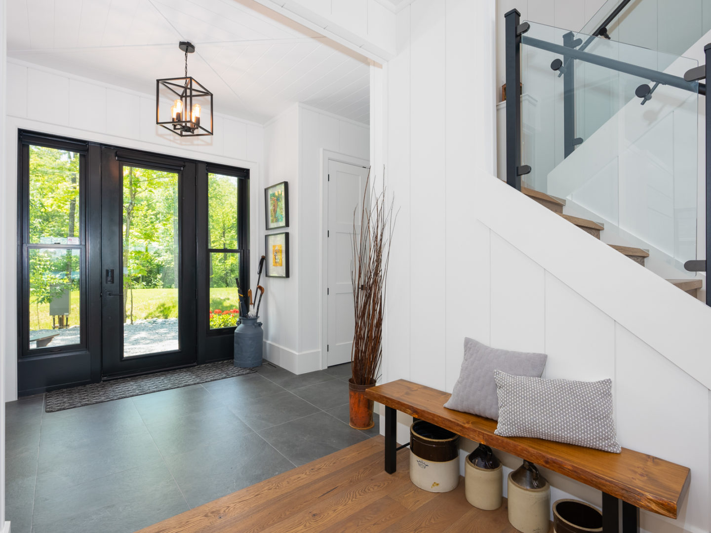 A large, bright entrance of a modern cottage, with white walls, a bench in the front hall, and stairs leading up off to the side.