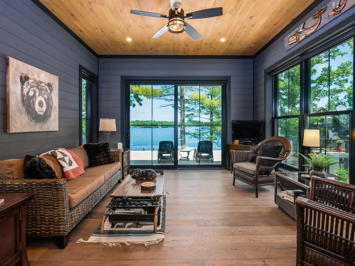 A living space in a sunroom with windows taking up each wall, a couch and chairs, and wooden floors.