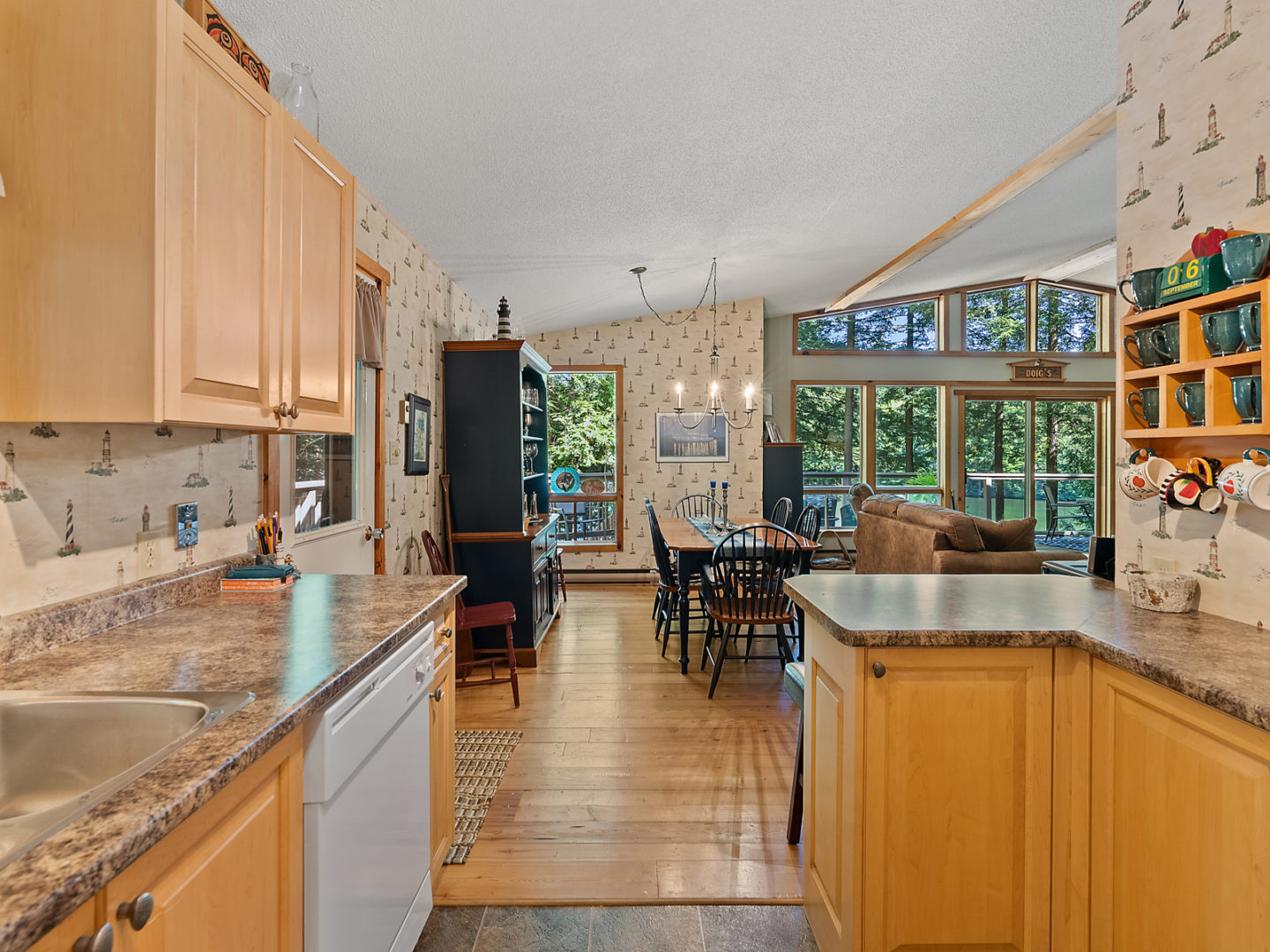 A modest kitchen with light wooden cabinets, looking out to an open-concept dining and living space.