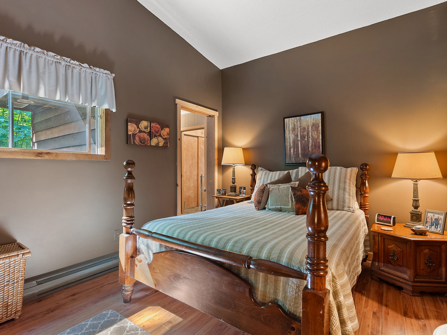 A spacious bedroom with a window and a bed that has a four-poster wooden bed frame.