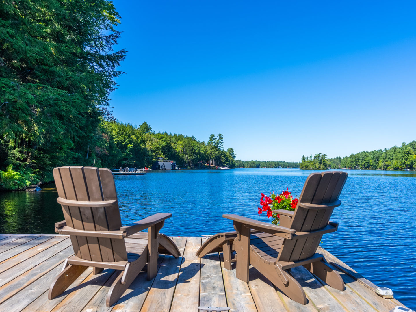 Two Muskoka chairs on the end of a dock, facing out toward a blue lake.