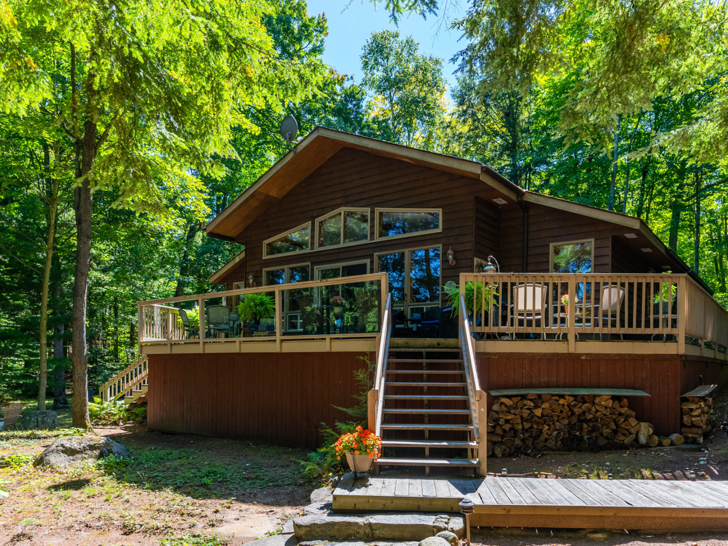 A wood frame cottage with steps leading up to a large deck, which branches off an exterior wall with large windows.