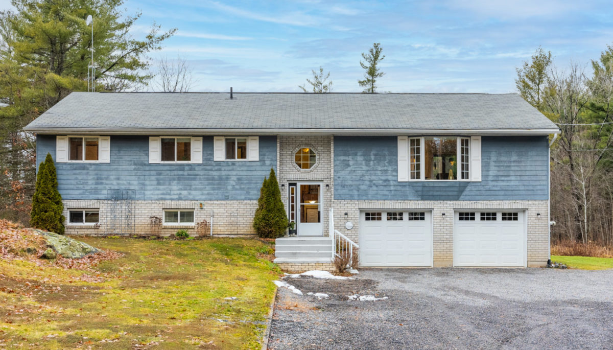 The front of a raised bungalow that has a light blue exterior and white garage doors.