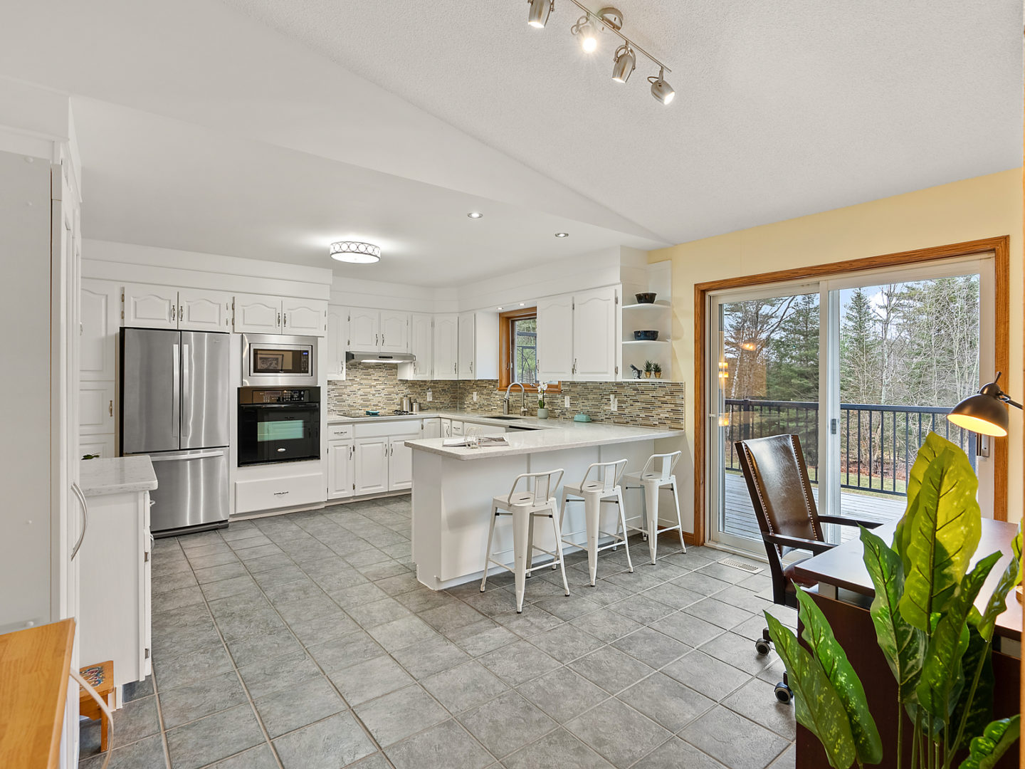 A large kitchen with tole flooring, white cupboards, and updated appliances.