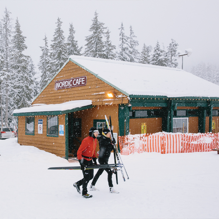 Two men holding skis walking past the cafe